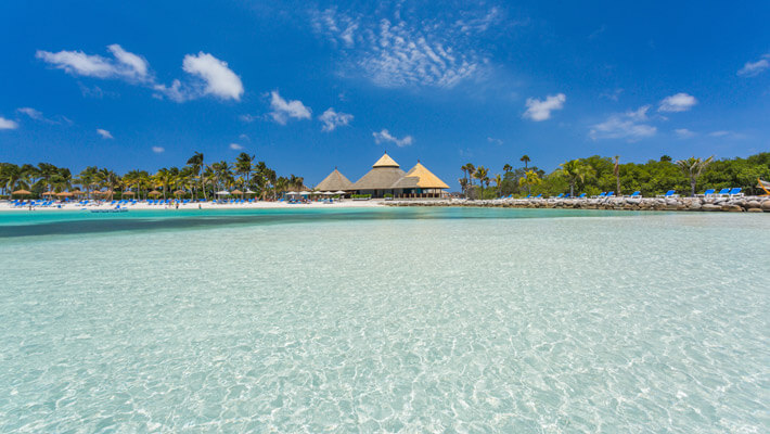 Playa Flamingo, Aruba Playa Flamingo tiene agua color turquesa cristalina y arena blanca, de fondo se observa grandes palmeras con kioscos para los turistas